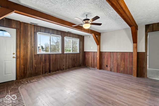 unfurnished room featuring wooden walls, ceiling fan, wood-type flooring, and a textured ceiling