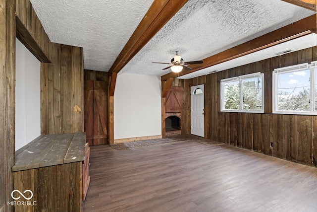 unfurnished living room featuring wood walls, a brick fireplace, dark hardwood / wood-style floors, ceiling fan, and a textured ceiling