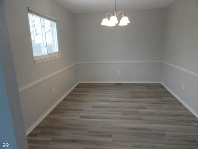 spare room with dark wood-type flooring and a notable chandelier