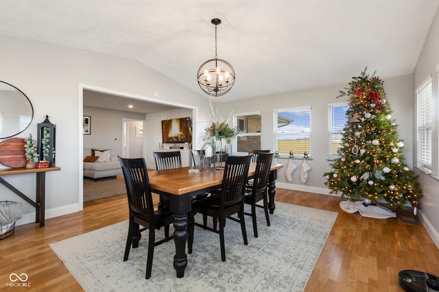 dining area with hardwood / wood-style flooring, a wealth of natural light, lofted ceiling, and a notable chandelier