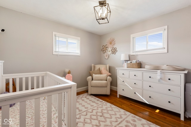 bedroom with dark hardwood / wood-style floors, a crib, a chandelier, and multiple windows