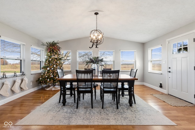 dining room with a textured ceiling, a chandelier, lofted ceiling, and light wood-type flooring