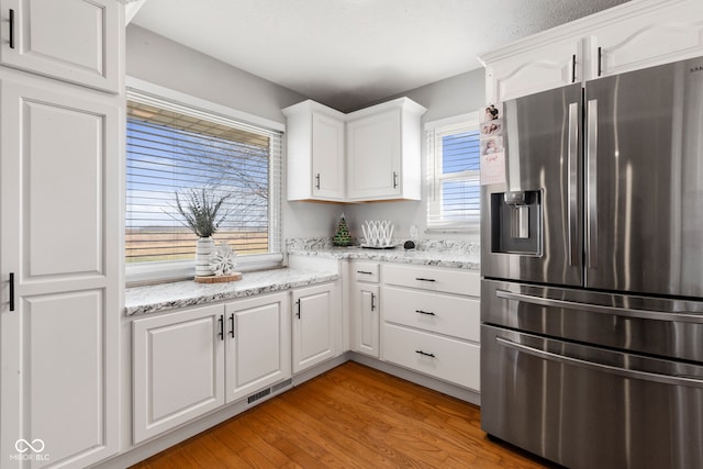 kitchen featuring a wealth of natural light, white cabinetry, stainless steel refrigerator with ice dispenser, and light wood-type flooring