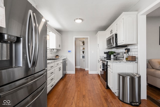 kitchen with sink, dark hardwood / wood-style floors, light stone counters, white cabinetry, and stainless steel appliances