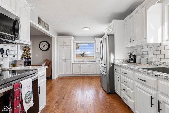 kitchen featuring wood-type flooring, light stone countertops, tasteful backsplash, white cabinetry, and stainless steel appliances