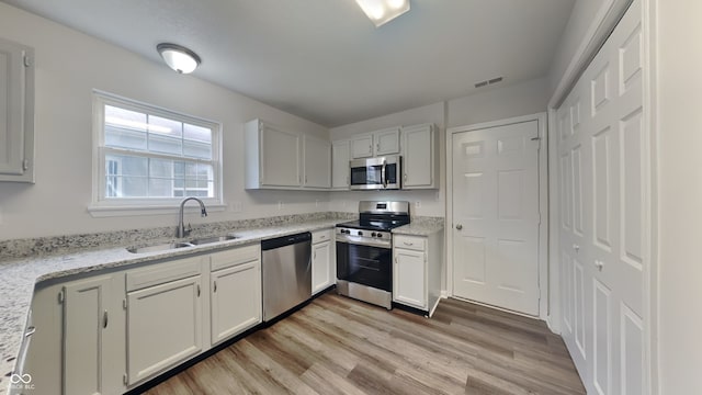 kitchen with appliances with stainless steel finishes, light wood-type flooring, white cabinetry, and sink