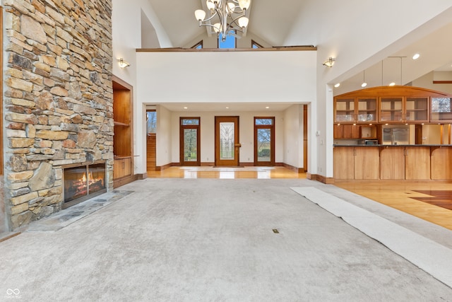 unfurnished living room with high vaulted ceiling, a notable chandelier, a fireplace, and light carpet