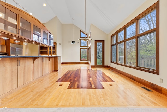 interior space with a kitchen breakfast bar, pendant lighting, high vaulted ceiling, light hardwood / wood-style flooring, and built in fridge