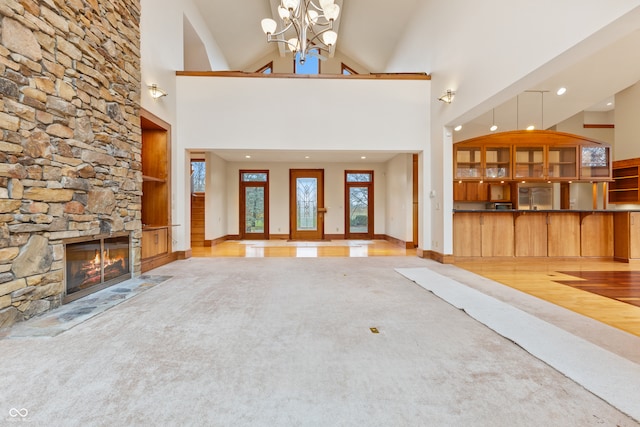 unfurnished living room with a fireplace, an inviting chandelier, high vaulted ceiling, and light wood-type flooring