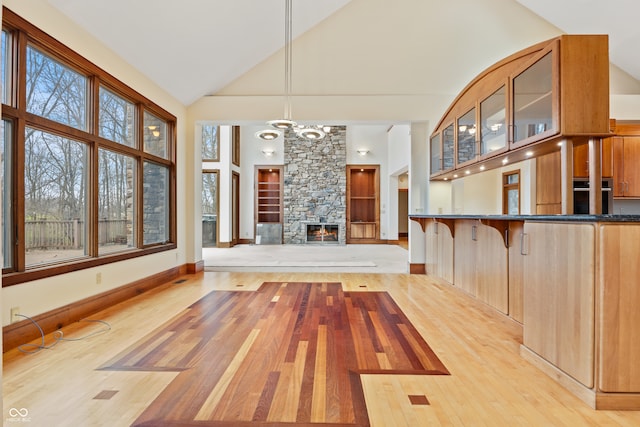 interior space featuring a fireplace, light wood-type flooring, a chandelier, and high vaulted ceiling