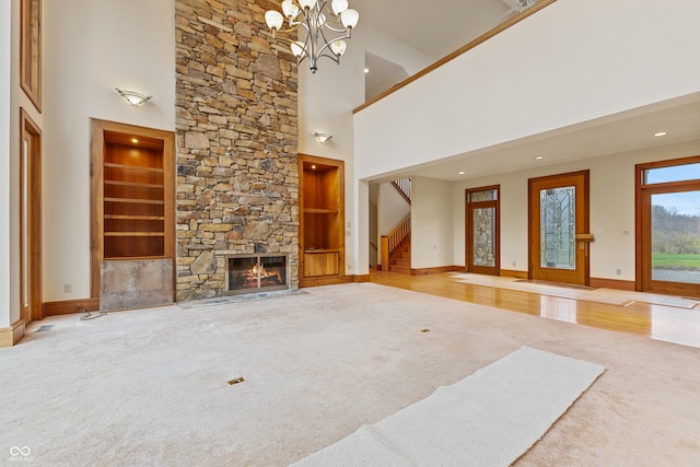 unfurnished living room featuring hardwood / wood-style floors, a high ceiling, an inviting chandelier, a stone fireplace, and built in shelves