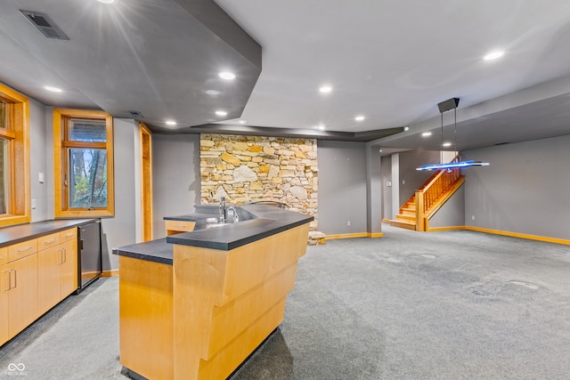 interior space with light carpet, light brown cabinets, an island with sink, and decorative light fixtures