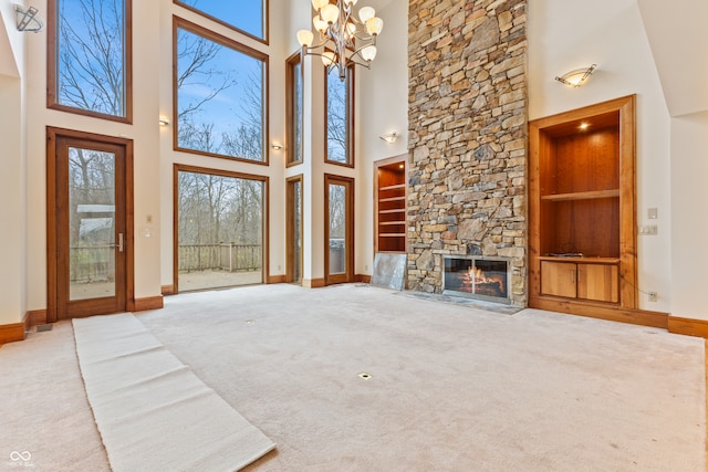 unfurnished living room with built in shelves, light colored carpet, a notable chandelier, a fireplace, and a high ceiling