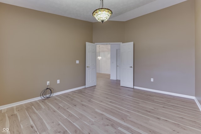 empty room featuring light hardwood / wood-style floors, a textured ceiling, and a notable chandelier