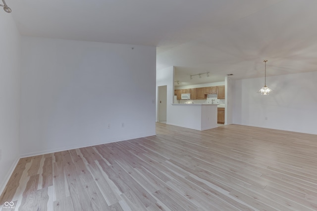 unfurnished living room with rail lighting, a chandelier, and light wood-type flooring