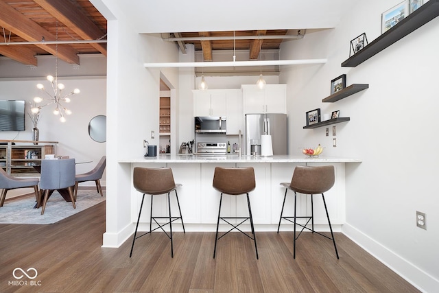 kitchen with white cabinets, dark hardwood / wood-style floors, a kitchen bar, kitchen peninsula, and stainless steel appliances