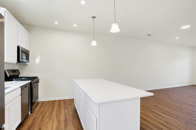 kitchen with appliances with stainless steel finishes, light wood-type flooring, decorative light fixtures, a center island, and white cabinetry