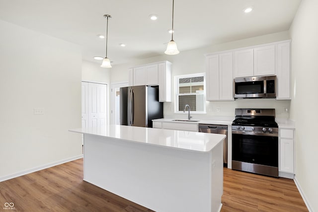 kitchen with appliances with stainless steel finishes, sink, white cabinets, a center island, and hanging light fixtures