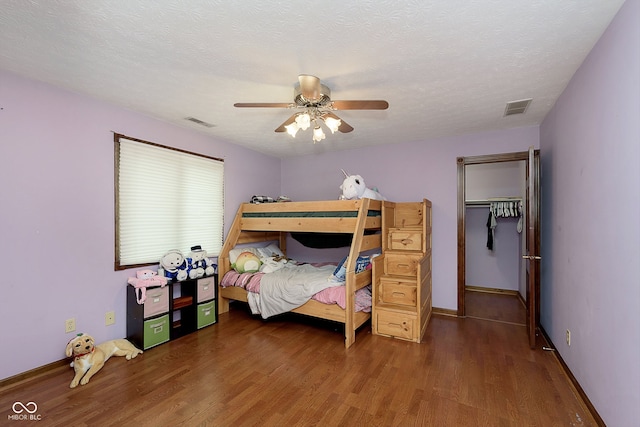 bedroom with a textured ceiling, a closet, dark hardwood / wood-style floors, and ceiling fan