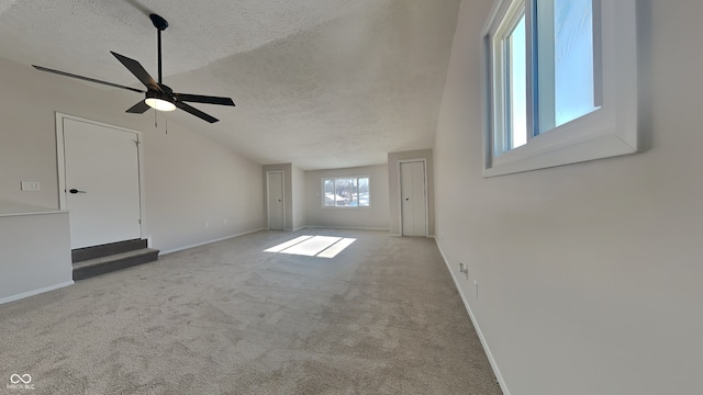 unfurnished living room with ceiling fan, vaulted ceiling, light carpet, and a textured ceiling