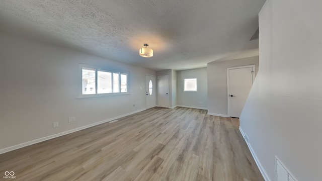 empty room with a textured ceiling and light hardwood / wood-style flooring