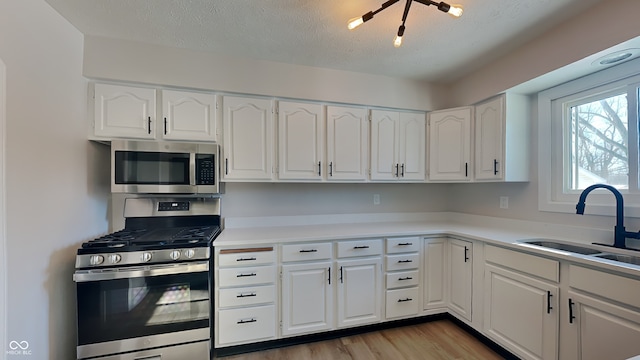 kitchen featuring sink, light hardwood / wood-style flooring, a textured ceiling, stainless steel appliances, and white cabinets