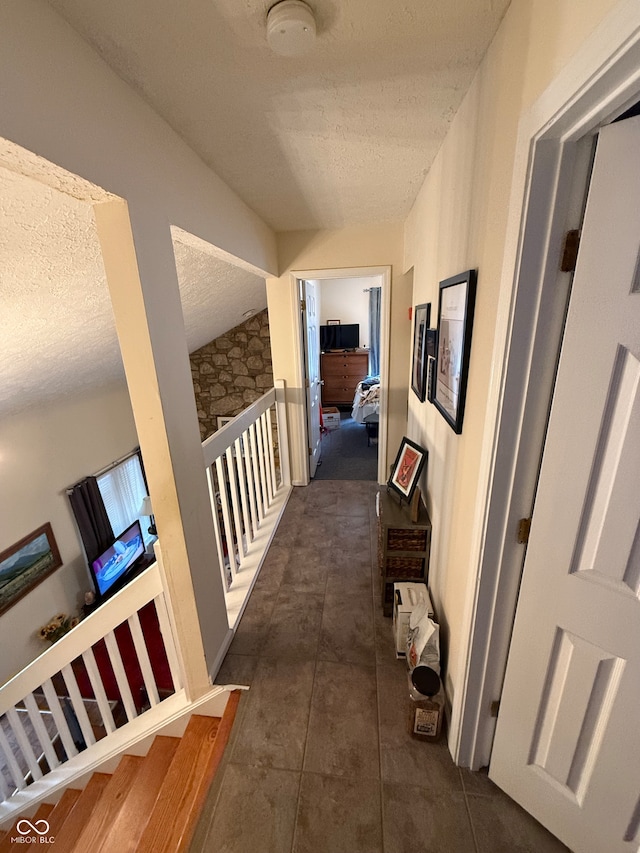 hallway with a textured ceiling, dark tile patterned floors, and lofted ceiling