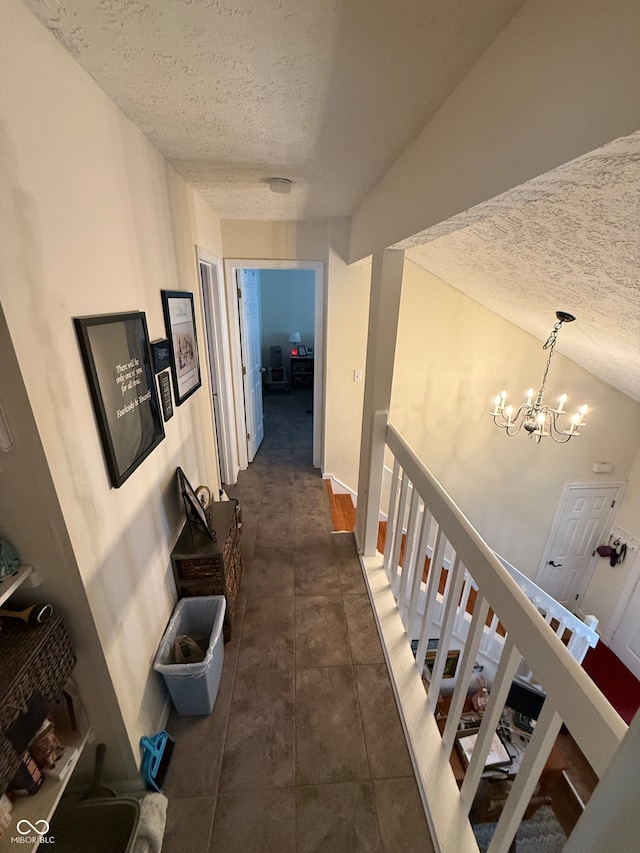 hallway featuring dark tile patterned flooring, a textured ceiling, vaulted ceiling, and a notable chandelier