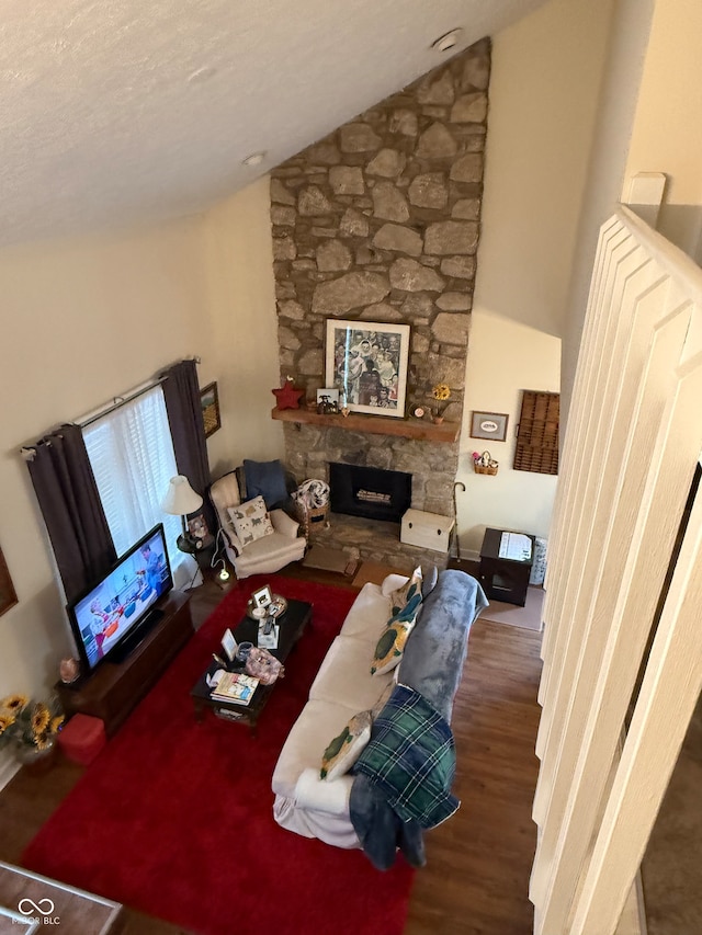 living room with a textured ceiling, a stone fireplace, dark wood-type flooring, and vaulted ceiling