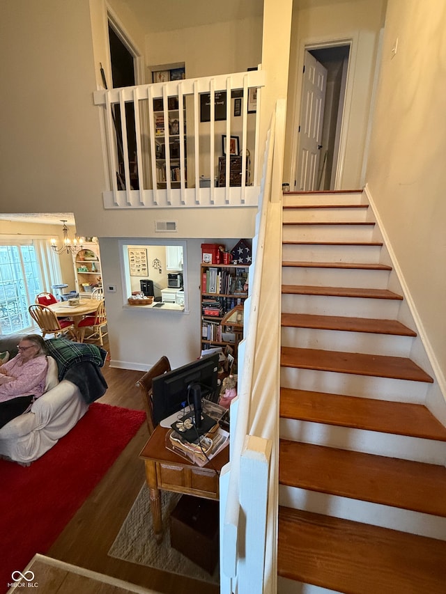 stairs featuring wood-type flooring and an inviting chandelier