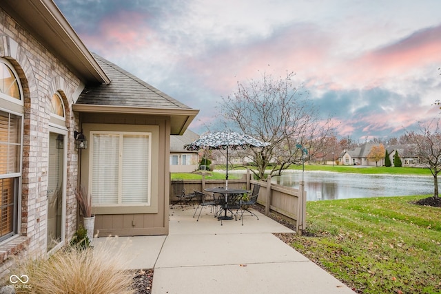 patio terrace at dusk featuring a lawn and a water view