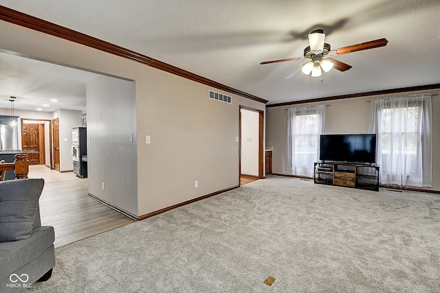 unfurnished living room with light carpet, a textured ceiling, ceiling fan, and crown molding