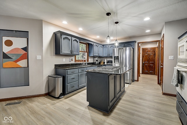 kitchen featuring appliances with stainless steel finishes, light wood-type flooring, sink, pendant lighting, and a center island