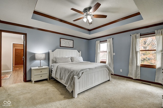 carpeted bedroom with a raised ceiling, multiple windows, ceiling fan, and crown molding