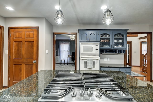 kitchen with wood-type flooring, dark stone countertops, white appliances, and hanging light fixtures