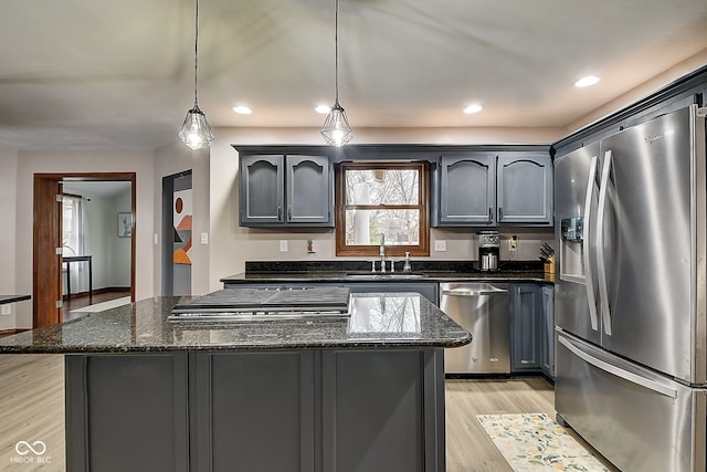 kitchen featuring appliances with stainless steel finishes, sink, decorative light fixtures, dark stone countertops, and light hardwood / wood-style floors