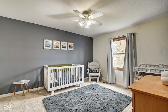 bedroom with a textured ceiling, a nursery area, light colored carpet, and ceiling fan