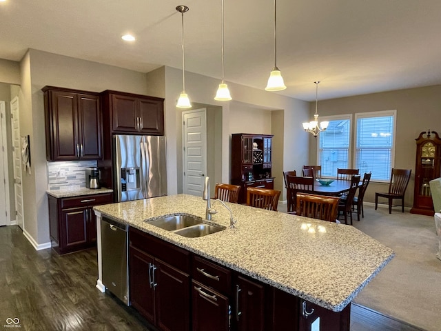 kitchen with dark brown cabinets, appliances with stainless steel finishes, sink, decorative light fixtures, and a center island with sink