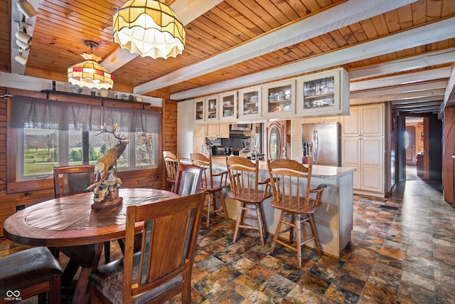 dining area featuring beam ceiling, track lighting, stone finish floor, wood walls, and wooden ceiling