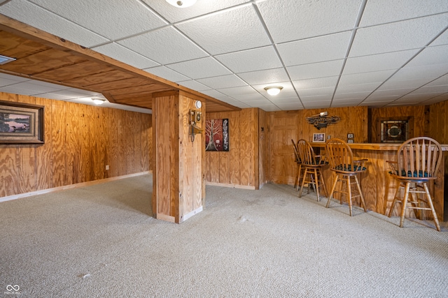 finished basement with wooden walls, carpet flooring, a bar, and baseboards