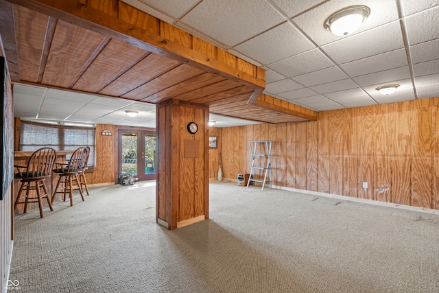 below grade area with wooden walls, carpet flooring, baseboards, and a drop ceiling