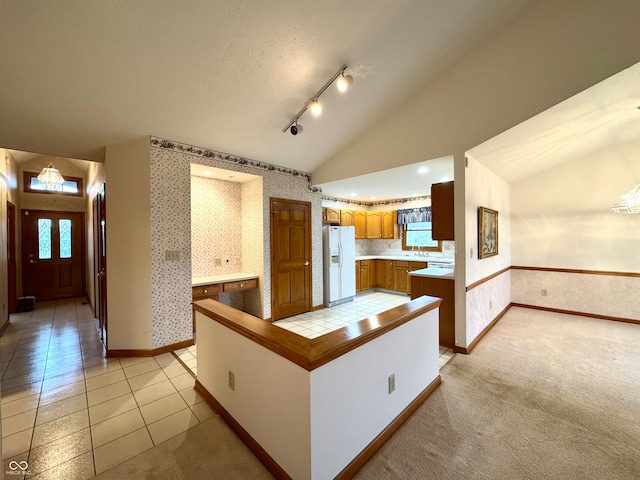 kitchen with track lighting, a textured ceiling, vaulted ceiling, light tile patterned floors, and white fridge with ice dispenser