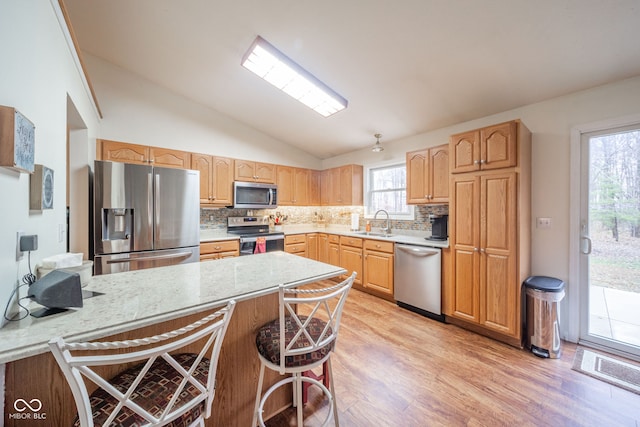 kitchen with sink, light hardwood / wood-style flooring, backsplash, lofted ceiling, and appliances with stainless steel finishes