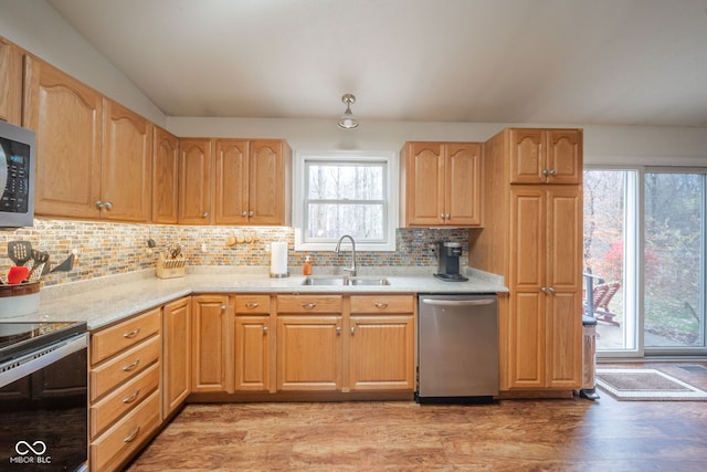 kitchen with sink, decorative backsplash, light wood-type flooring, light stone counters, and stainless steel appliances