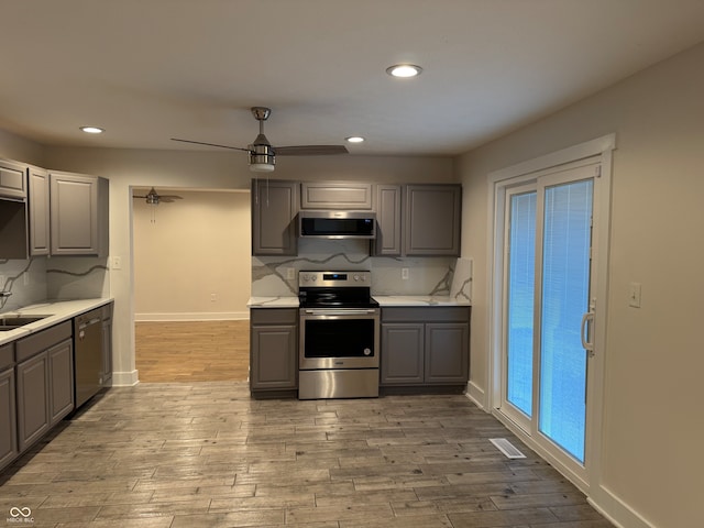 kitchen featuring tasteful backsplash, light hardwood / wood-style floors, extractor fan, gray cabinets, and appliances with stainless steel finishes