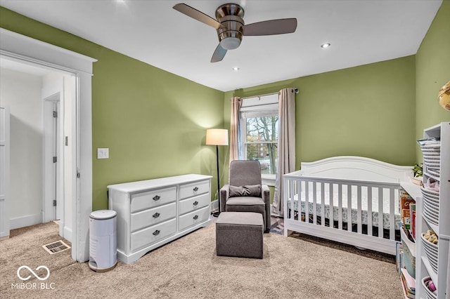 carpeted bedroom featuring ceiling fan and a crib