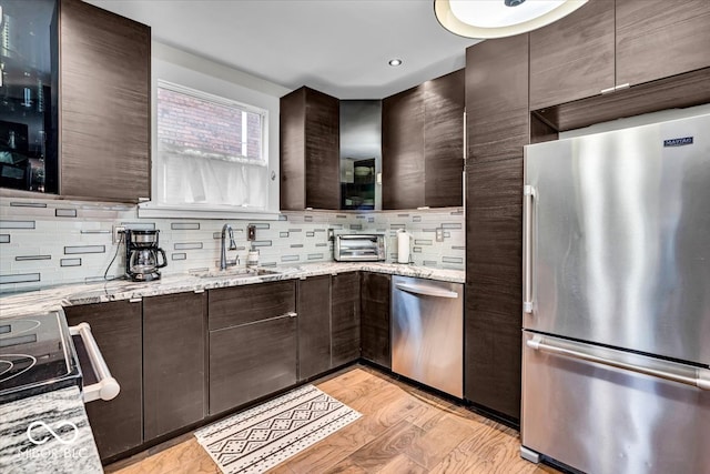 kitchen featuring appliances with stainless steel finishes, light stone counters, dark brown cabinetry, sink, and light hardwood / wood-style floors