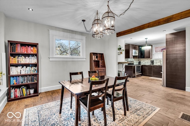 dining space featuring beam ceiling, light hardwood / wood-style floors, and an inviting chandelier