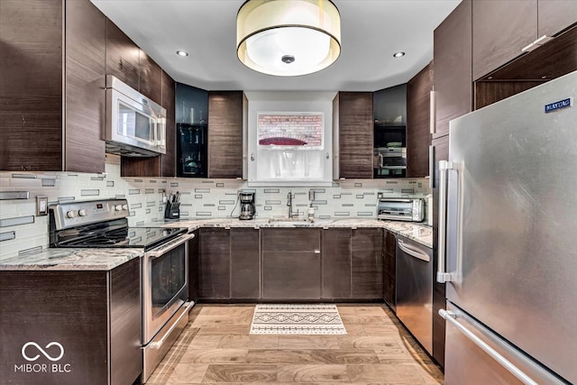 kitchen featuring light stone countertops, light wood-type flooring, backsplash, and appliances with stainless steel finishes