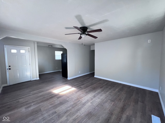 unfurnished living room with visible vents, baseboards, dark wood finished floors, arched walkways, and ceiling fan